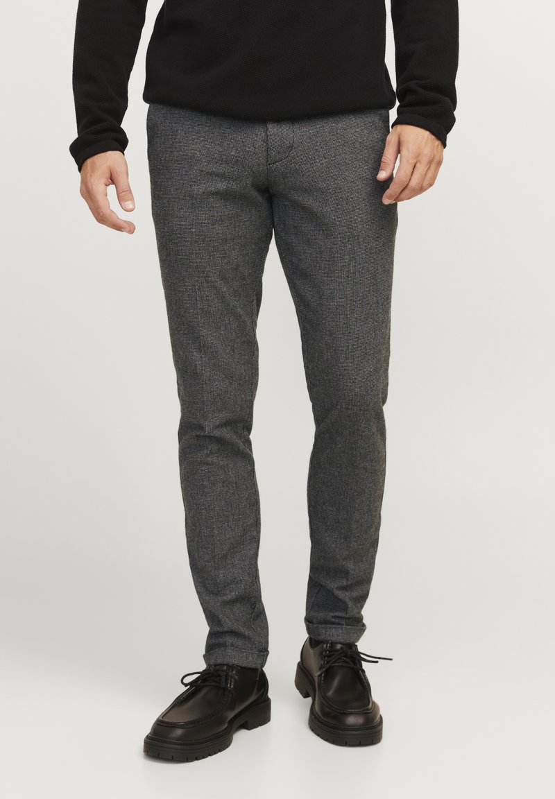 Grau gemusterte, texturierte Hose mit schmalem Schnitt und mittelhohem Bund, kombiniert mit schwarzen Schnürschuhen.
