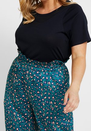 T-shirt noire à manches courtes associée à un pantalon bleu sarcelle orné d'un motif léopard rose et marine, avec une taille élastique à volants.