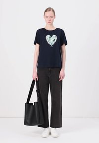 Námořnické bavlněné tričko s stylizovaným světle zeleným srdcem, kombinované s černými širokými džínami a černou taškou. Bílá sneakers dotvářejí vzhled.