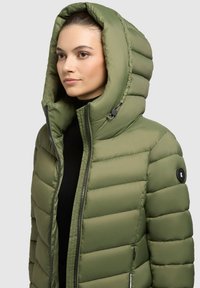 Puffjakke i olivengrøn, med stort hætte, quiltet design, frontlynlås og sidelommer; lavet af let, glat stof.