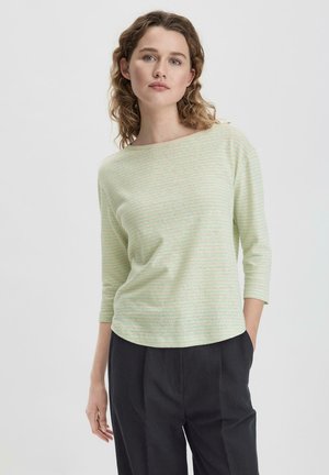 Haut à rayures vert clair avec un décolleté bateau, des manches trois-quarts et une texture douce, associé à un pantalon sombre.