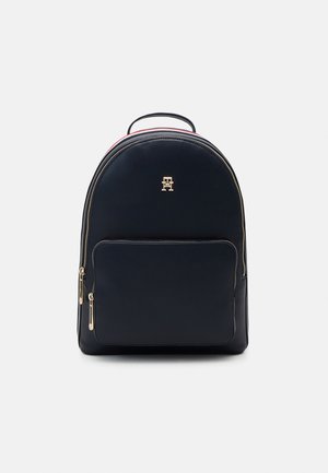 Zaino in pelle blu navy con dettagli in metallo dorato, forma arrotondata e chiusura con doppia cerniera. Presenta una tasca frontale e una maniglia superiore per il trasporto.