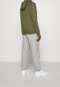 Olivgrön huvtröja kombinerad med ljusgrå cargobyxor. Skorna är vita sneakers. Enkel design med avslappnad passform.