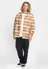 Meerkleurig patroonhemd met een knoopsluiting, met oranje, gele en blauwe tinten; gecombineerd met zwarte jeans in relaxed fit en sneakers.