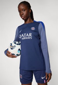 Marinblå langermet trøye med blå detaljer, med "Qatar Airways" logo; matchende short; holder en mønstrete fotball.