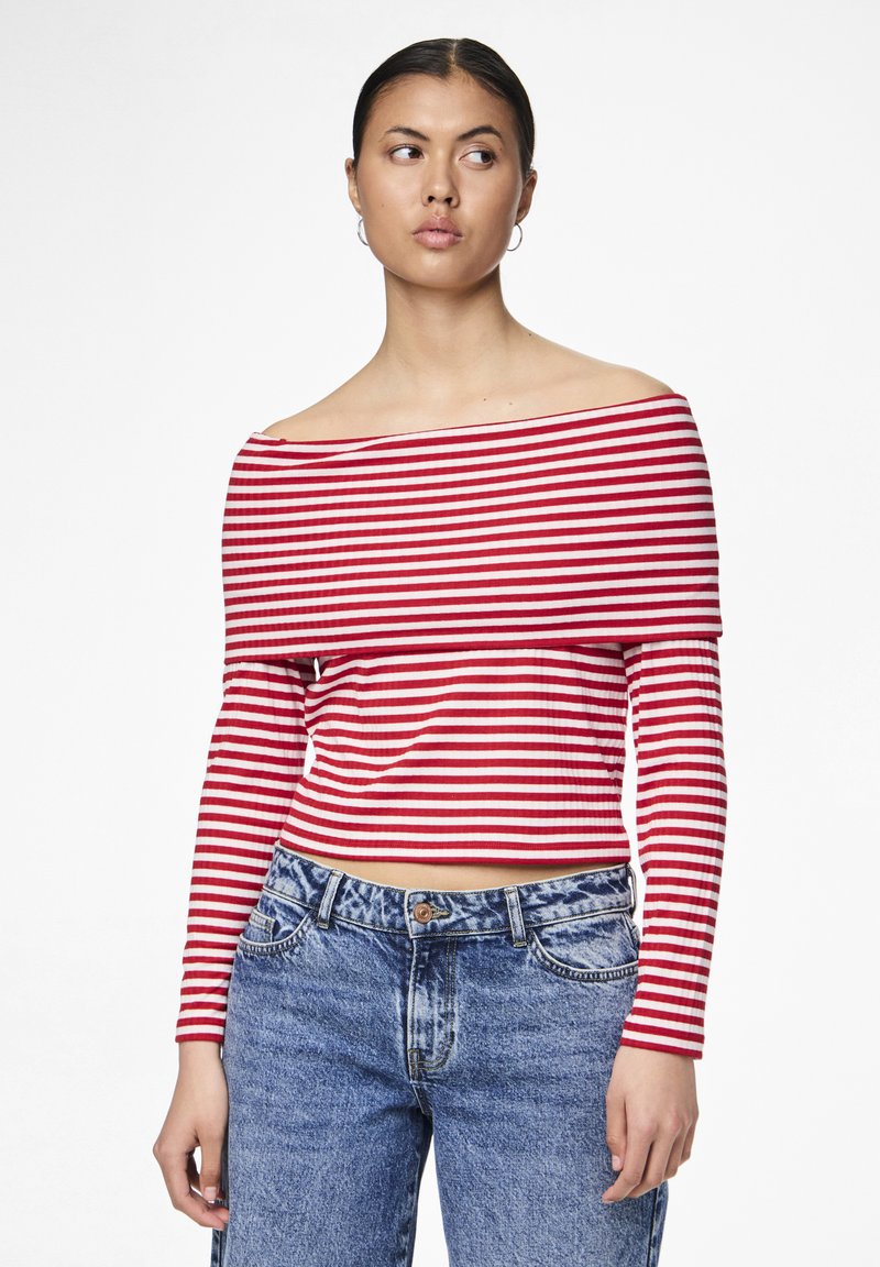 Skulder-underdel, langermet topp med røde og hvite horisontale striper. Stoffet ser mykt ut med en tettsittende design. Sammen med høytlivs blå jeans.