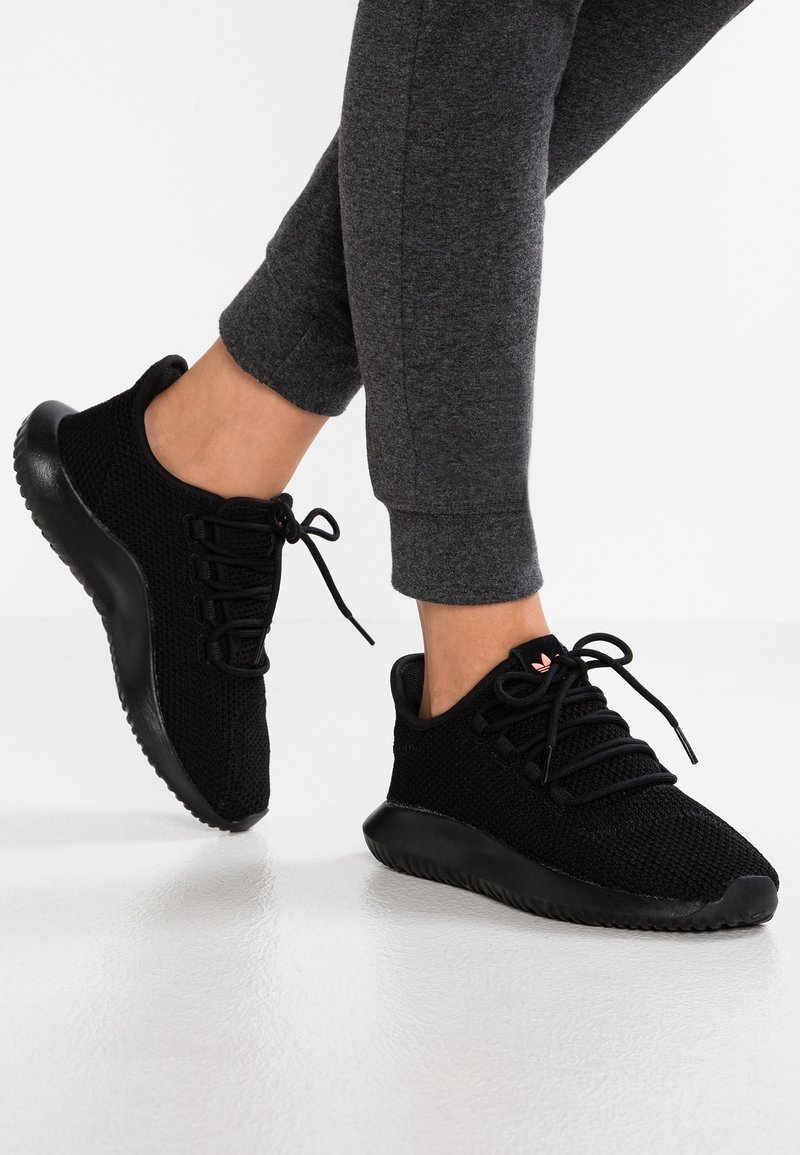 Svarta sportskor med en stickad ovandel, rund tå och strukturerad sula. Har snörning och diskret logotyp på tungan.
