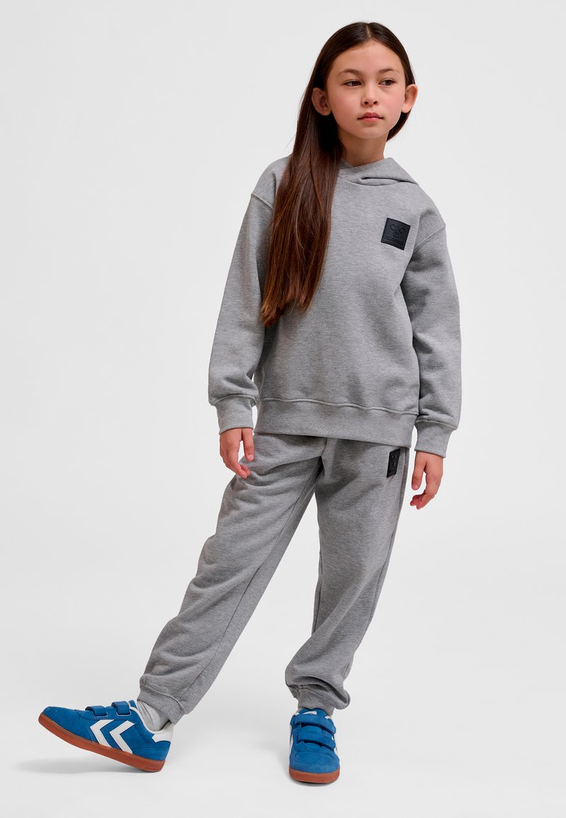 Grå huvtröja med huva och framficka, ihop med matchande joggerbyxor, kompletterad med blå sneakers med vita detaljer.
