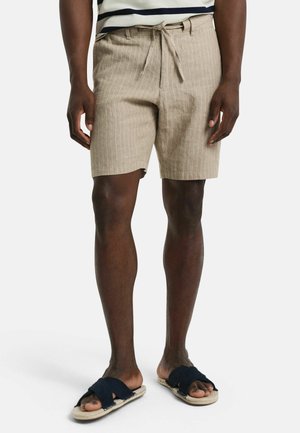 Beige striped shorts made from lightweight fabric, featuring a drawstring waist and side pockets, paired with dark slip-on sandals.
