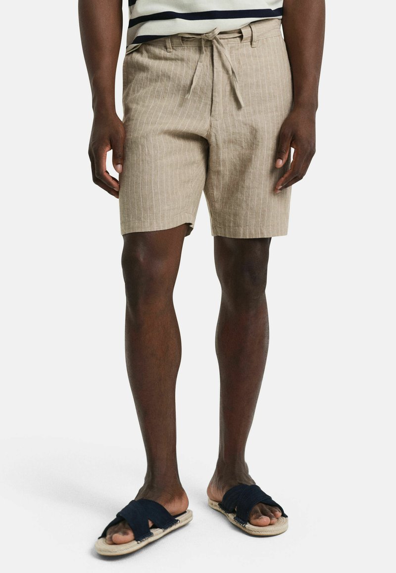 Beige gestreepte shorts gemaakt van lichte stof, met een drawstring taille en zijzakken, gecombineerd met donkere instapsandalen.
