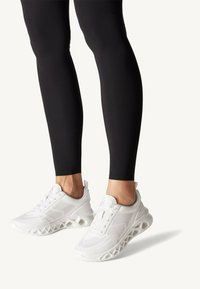 Valged spordijalatsid, millel on hingav võrkkangas pealisosa ja ainulaadne lõigetega talvekujundus. Kanda istuvate mustade retuusidega, rõhutades kingade detaile.