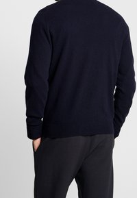 Marinblått stickat tröja med rund halsringning, ribbade ärmslut och nederkant. Mjuk textur och ledig passform, bärs med mörka byxor. Enkel, klassisk design.