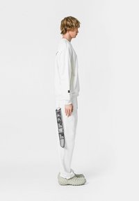 Sudadera blanca y pantalones con detalles impresos en el costado, combinados con calzado texturizado gris, mostrados en vista lateral.