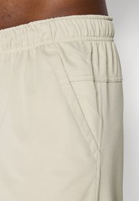 Helle beigefarbene Shorts aus strukturiertem Stoff, mit einem elastischen Bund und einer seitlichen Tasche mit flacher Naht.