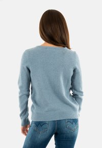 Maglione azzurro chiaro in maglia morbida con maniche lunghe e scollatura rotonda. Orlo e polsini a coste. Indossato con jeans aderenti.
