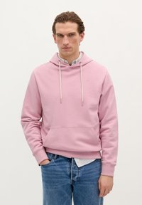 Lichtroze hoodie met een trekkoordkap, een voorzak, ribgebreide manchetten en zoom. Draagt over een overhemd met kraag en gecombineerd met blauwe jeans.