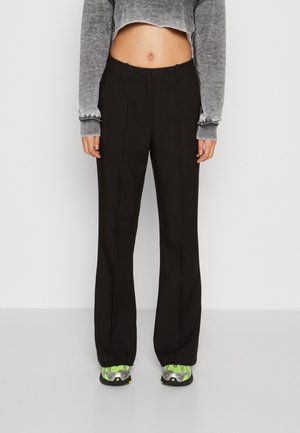 Person wearing black straight pants, gray long-sleeve cropped top, and green and gray sneakers standing against a plain background.