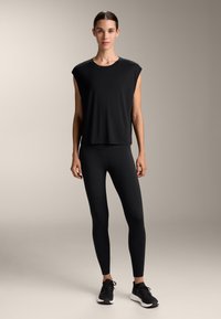 Top nero a maniche corte con una vestibilità ampia, abbinato a leggings neri e sneakers nere. Tessuto liscio, design minimale, senza motivi visibili.
