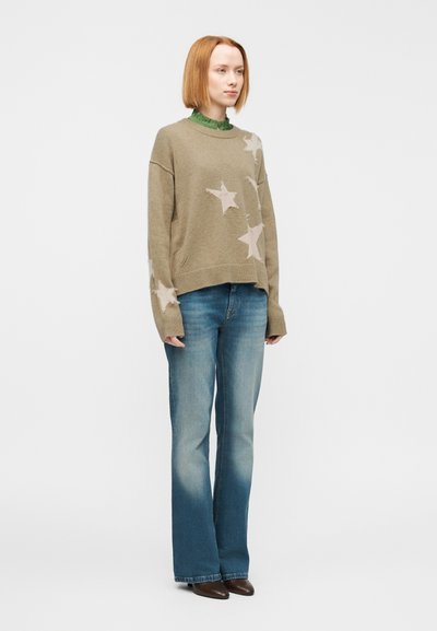 Πουλόβερ σε χρώμα ελιάς με μπεζ σχέδιο αστέρι, άνετη γραμμή, ριμπ λαιμόκοψη. Συνδυασμένο με ανοιχτό μπλε καμπάνα τζιν και καφέ παπούτσια με τακούνι.