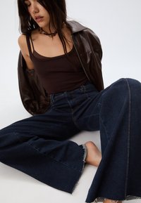 Temno modre široke jeans hlače s razfrkanimi robovi, v kombinaciji z oprijetim rjavim topom in rjavim usnjenim jopičem.