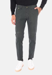 Chinos da uomo verde scuro in un tessuto leggero, caratterizzati da una vestibilità slim, due tasche anteriori, chiusura con bottone, abbinati a sneakers bianche.
