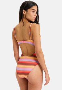 Kleurrijk gestreept zwemkleding gemaakt van een textuur, ribbelstof. Heeft een lage rugontwerp en dunne verstelbare bandjes in tinten roze, oranje en bruin.