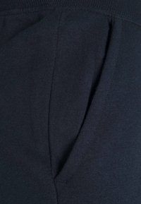 Lähikuva tummansinisestä kankaasta, jossa on pystysuora tasku näkyvällä ompeleella ja ribbikuvioinnilla.