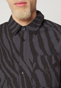 Svart- och grårandig skjorta med knappar vid kragen, framficka med en broderad logotyp och subtil textur.