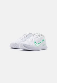 Bílé sportovní boty s texturovaným síťovaným svrškem, zeleným znakem swoosh a gumovou podrážkou. Obsahují šněrovací systém a minimální branding po straně.