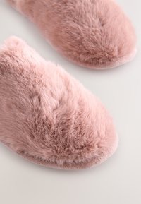 Chaussons en fausse fourrure rose avec un bout arrondi et une texture douce et moelleuse ; semelle en caoutchouc offrant stabilité et adhérence.