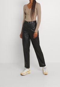 Bruine geribbelde lange mouw top met een V-hals en ritsdetail, gecombineerd met hoge zwarte leren broeken en lichte sneakers.