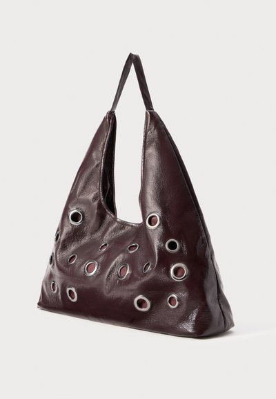 Burgundia nahast kott, millel on lõtv siluett, ringikujuliste lõigetega kontrastsetes äärtes ja ülemine käepide kandmiseks.