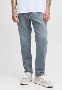 Jeans de mezclilla gris claro con corte recto, que presentan costuras visibles y una textura ligeramente deslavada. Combinados con zapatillas neutras.