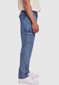 Pantalones cargo de denim en azul claro con un diseño de pierna recta, que cuentan con dos bolsillos laterales y bolsillos traseros adicionales, combinados con zapatillas blancas.