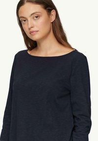 Langarmtop in donkerblauw, gemaakt van gestructureerde stof met een brede ronde halslijn. Het ontwerp heeft een lichte draping en minimale naden.