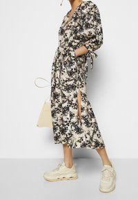 Kreemivärviline lilleline midi kleit, musta ja beeži detailidega. Omab V-kaelust, nööriga varrukaid, külgmisi lõhke ja on kombineeritud beežide tossudega.