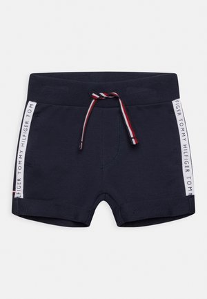 Pantalones cortos de niño pequeño azul marino con dobladillos enrollados, cordón a rayas y paneles laterales blancos con el texto "Tommy Hilfiger".