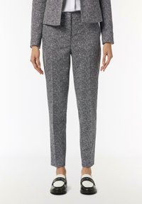 Strukturierte Hahnentritthosen in Schwarz und Weiß, schmal zulaufende Passform, mittelhoher Bund, kombiniert mit schwarz-weißen Slippern. Glatte Stoffoberfläche.