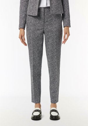 Strukturierte Hahnentritthosen in Schwarz und Weiß, schmal zulaufende Passform, mittelhoher Bund, kombiniert mit schwarz-weißen Slippern. Glatte Stoffoberfläche.