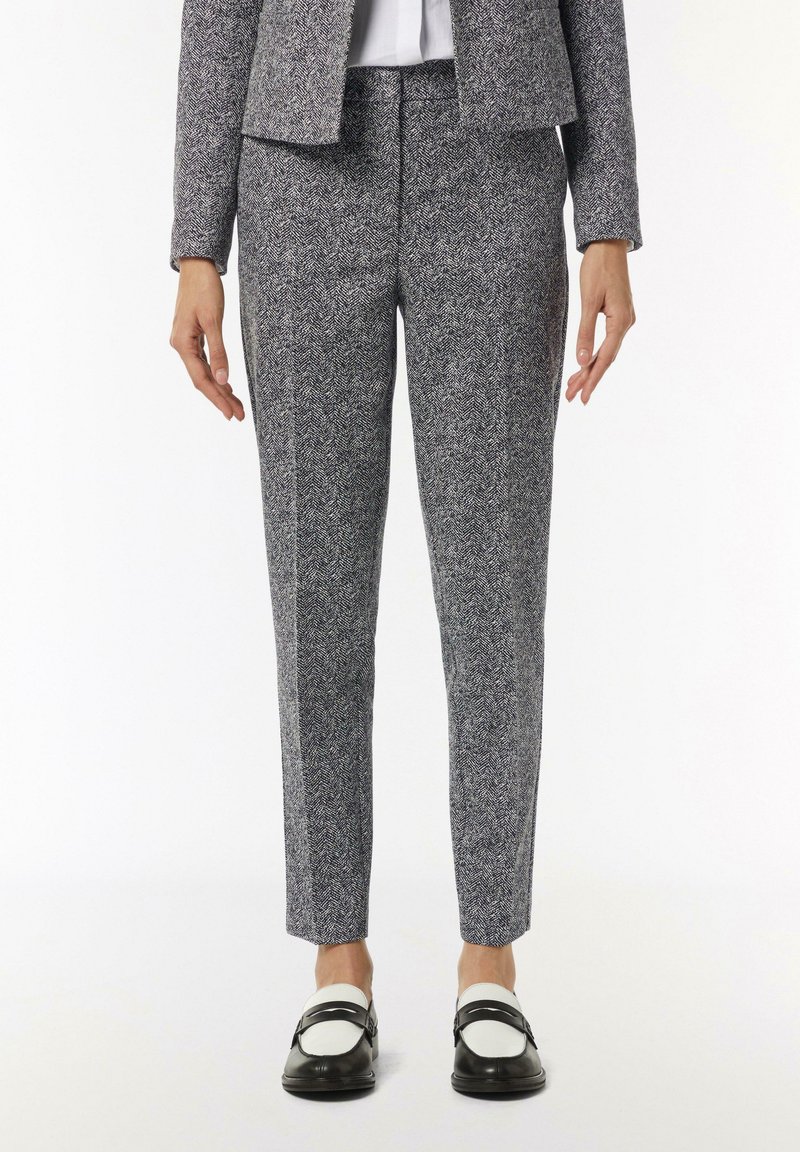 Strukturierte Hahnentritthosen in Schwarz und Weiß, schmal zulaufende Passform, mittelhoher Bund, kombiniert mit schwarz-weißen Slippern. Glatte Stoffoberfläche.