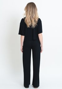 Svart kortärmad topp som matchas med svarta vida byxor. Tyget verkar mjukt, med en slät textur och minimal detaljer.