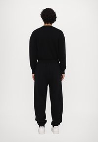 Schwarzes Sweatshirt- und Jogginghosen-Set mit lockerer Passform. Die Jogginghosen haben einen elastischen Bund und Bündchen an den Knöcheln, ergänzt durch weiße Turnschuhe.