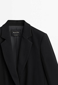 Zwarte blazer met scherpe revers, gestructureerde vorm, gladde stof en een intern label met de tekst "Massimo Dutti." Gemaakt in Portugal.