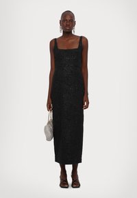 Schwarzes Spitzen-Midi-Kleid mit quadratischem Ausschnitt, schmalen Schulterträgern und gerader Silhouette. Kombiniert mit einer silbernen Handtasche und schwarzen Sandaletten.