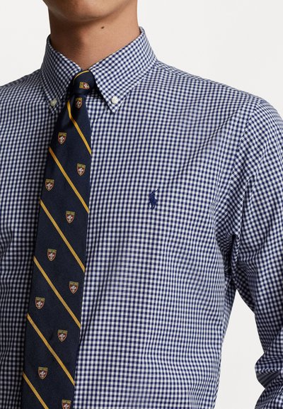 Marineblauwe en witte geblokte overhemden met button-down kraag, gecombineerd met een gestreepte das met schildlogo's op diagonale lijnen.