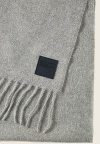 Grijze wollen sjaal met franjes aan de uiteinden en een zwart leren label met reliëftekst, die een zachte textuur en een rechthoekige vorm benadrukt.