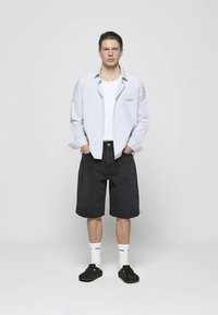 Gestreepte langlopende shirt, witte T-shirt, zwarte denim shorts. Accessoires omvatten witte sokken en donkere klompen. Eenvoudig ontwerp en ontspannen pasvorm.