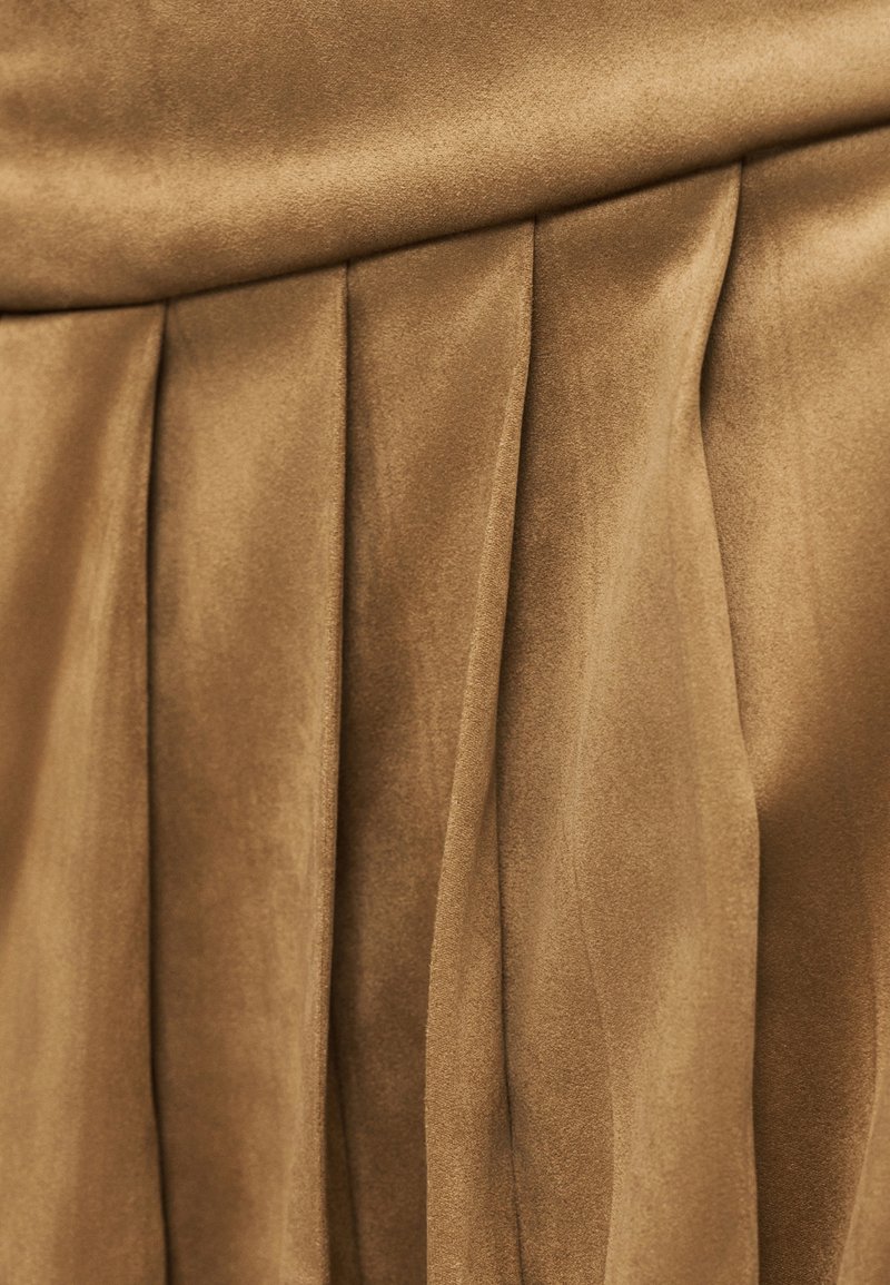 Jupe plissée d'un riche ton brun, confectionnée dans un tissu doux et lisse avec une légère brillance. Présente des plis verticaux créant texture et mouvement.