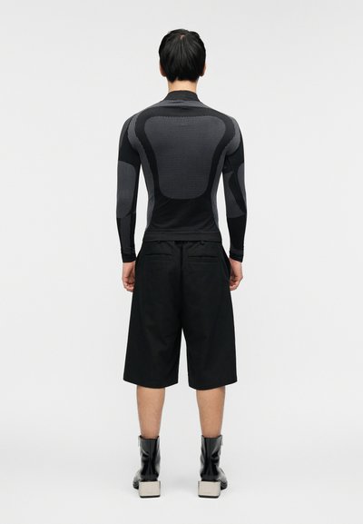 Μαύρο αθλητικό τοπ με μακριά μανίκια και υφασμάτινες υφές, σε συνδυασμό με μαύρες βερμούδες μήκους μέχρι το γόνατο και μαύρα μποτάκια με τετράγωνες ψηλές σόλες.