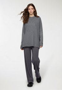 Szary sweter o fakturze z luźnym krojem, w zestawieniu z ciemnoszarymi szerokimi spodniami z prążkowanej dzianiny oraz czarnymi butami wsuwanymi.